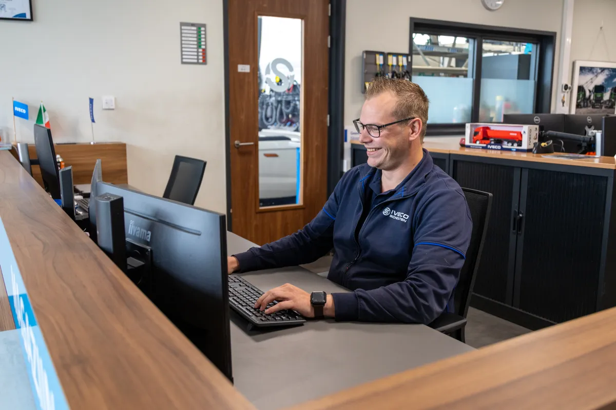 Servicemedewerker in IVECO Schouten-bedrijfskleding glimlachend aan de balie.