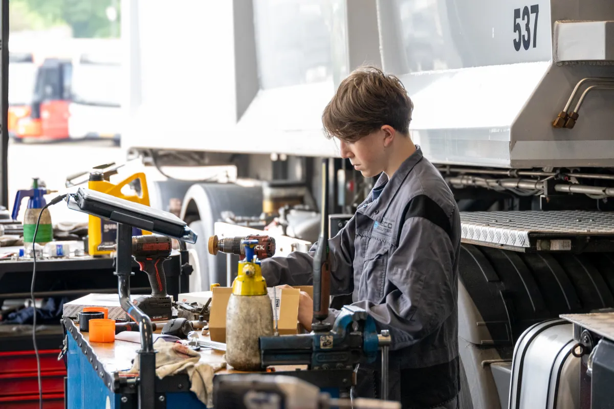 Jonge monteur werkt aan de werkbank naast een vrachtwagen.