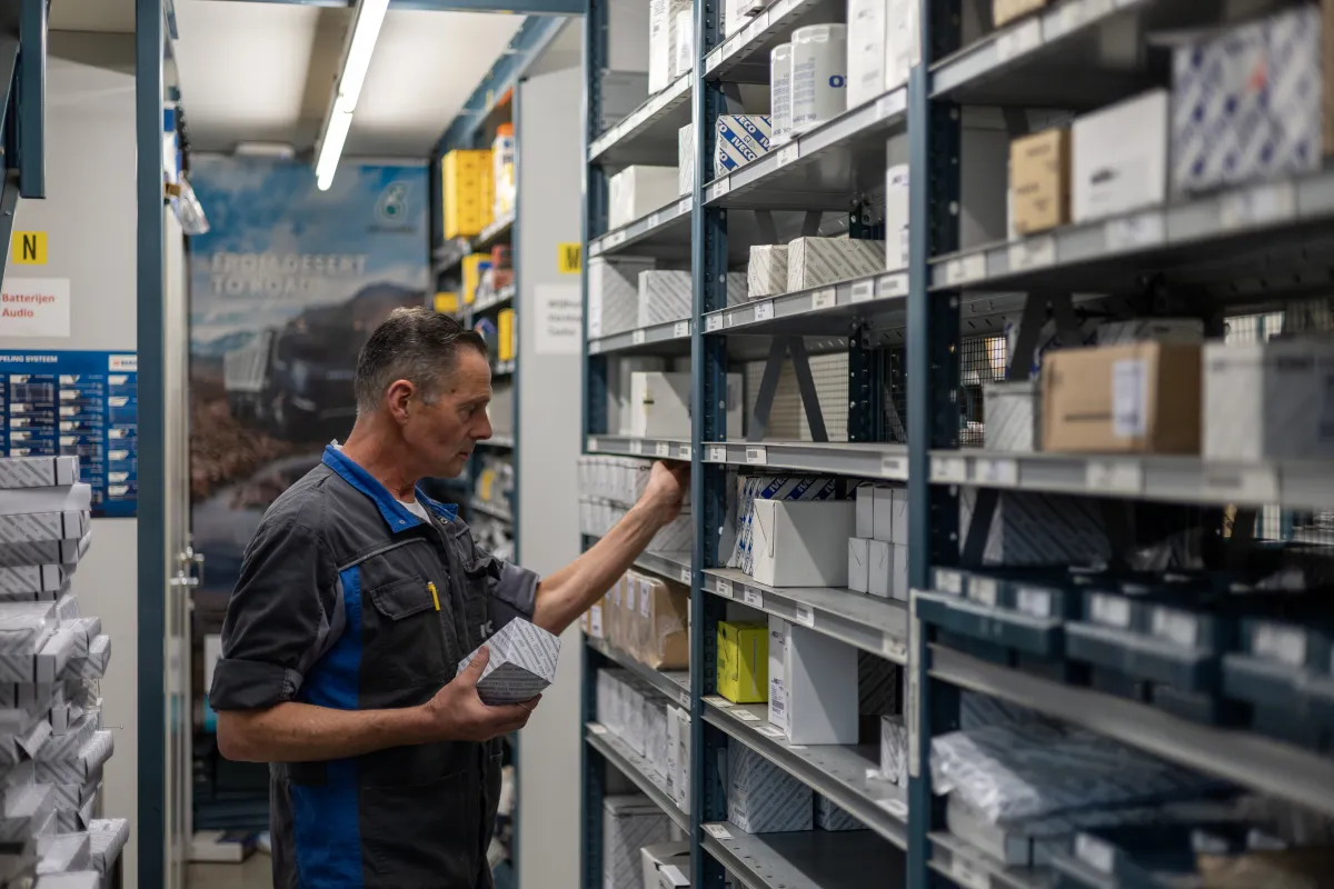 Magazijnmedewerker in oude IVECO-werkkleding pakt een onderdeel uit de stelling.