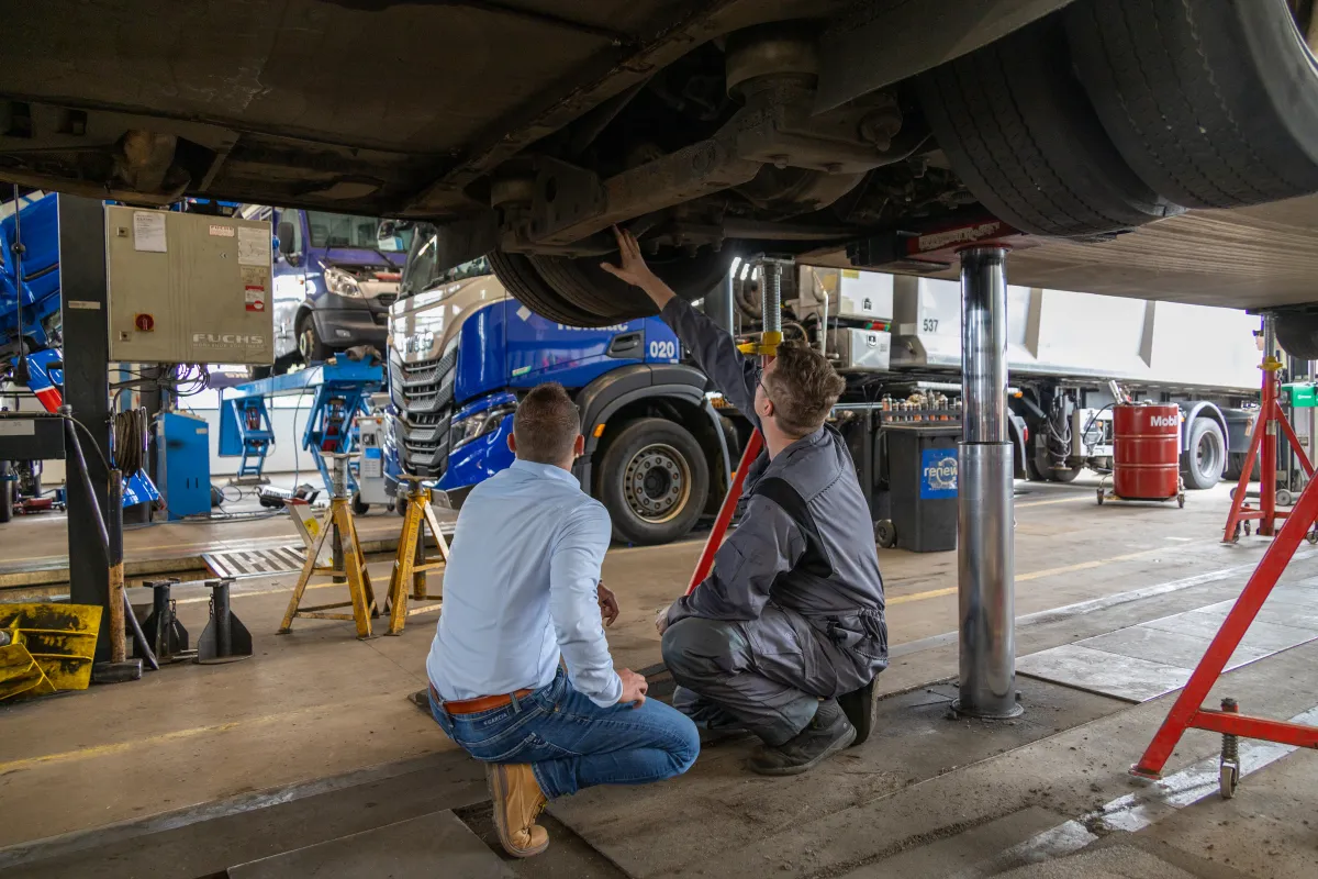 Serviceadviseur en monteur gehurkt onder een vrachtwagen op de hefbrug.