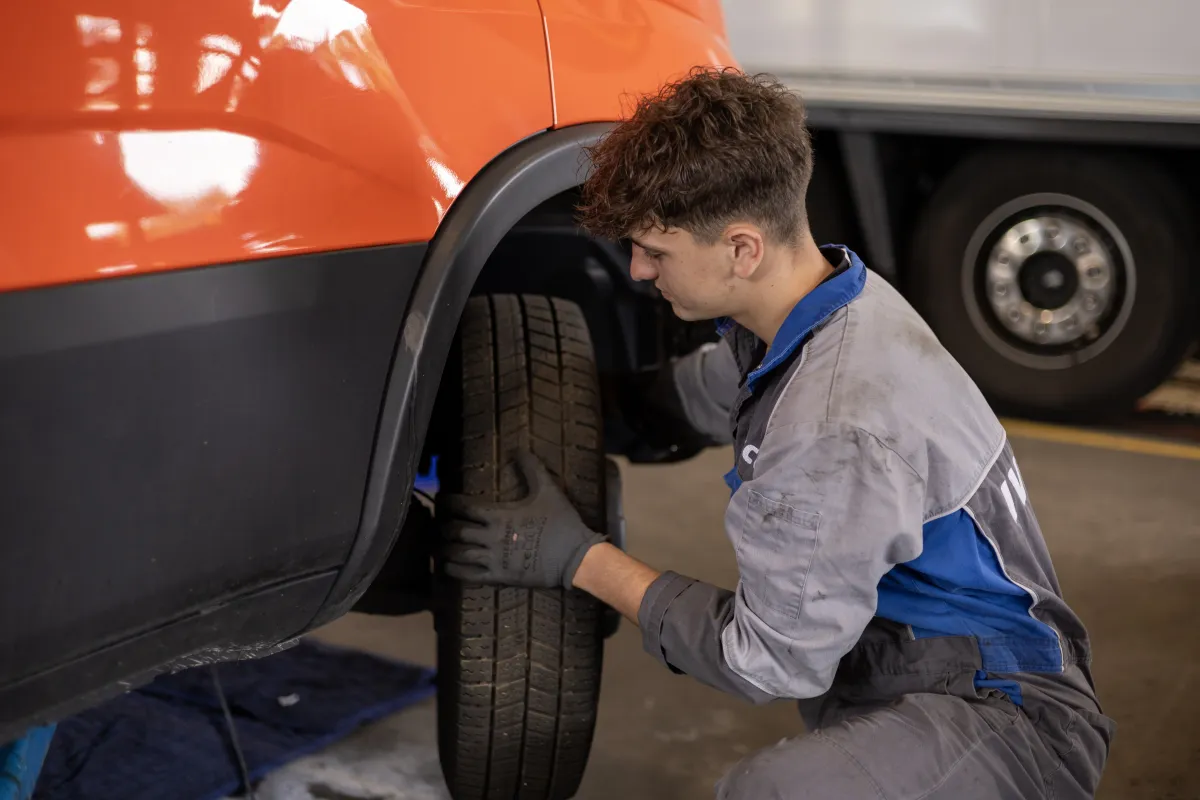Monteur in oude IVECO-werkkleding werkt aan de band van een oranje bestelwagen.