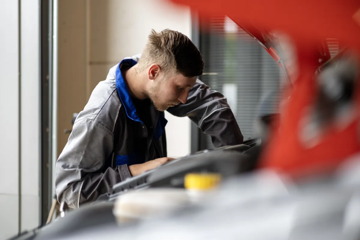 Monteur in oude IVECO-werkkleding werkt aan een geopende motorruimte.