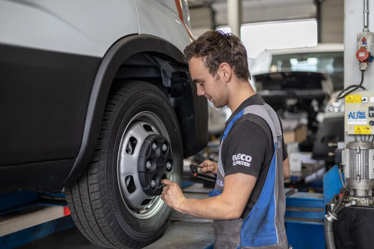Monteur werkt aan het wiel van een opgehesen bestelwagen.