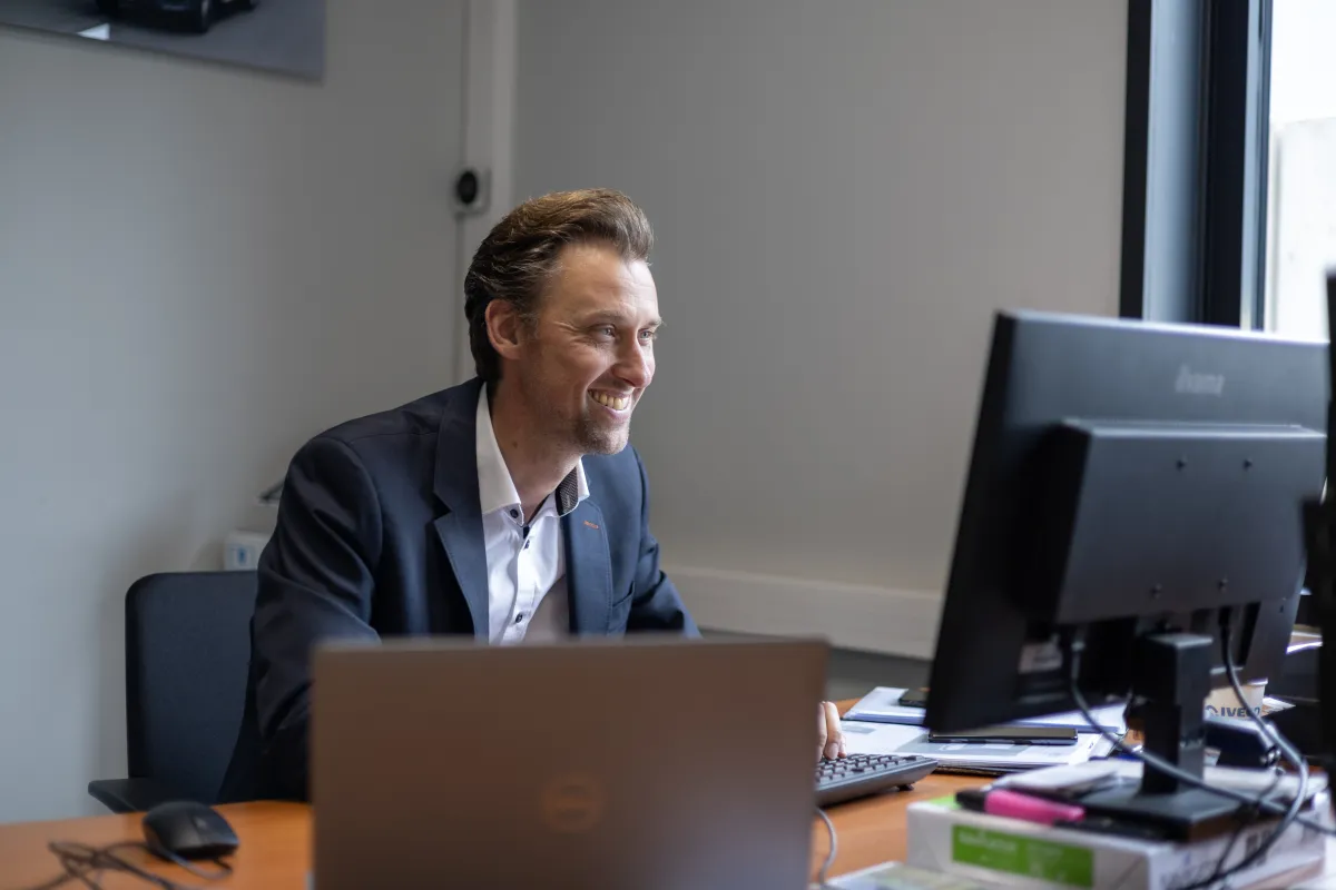 Accountmanager in colbert glimlachend achter het bureau.