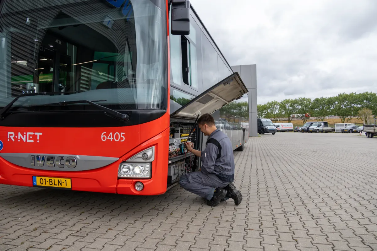 Monteur werkt buiten aan rode bus en lacht.