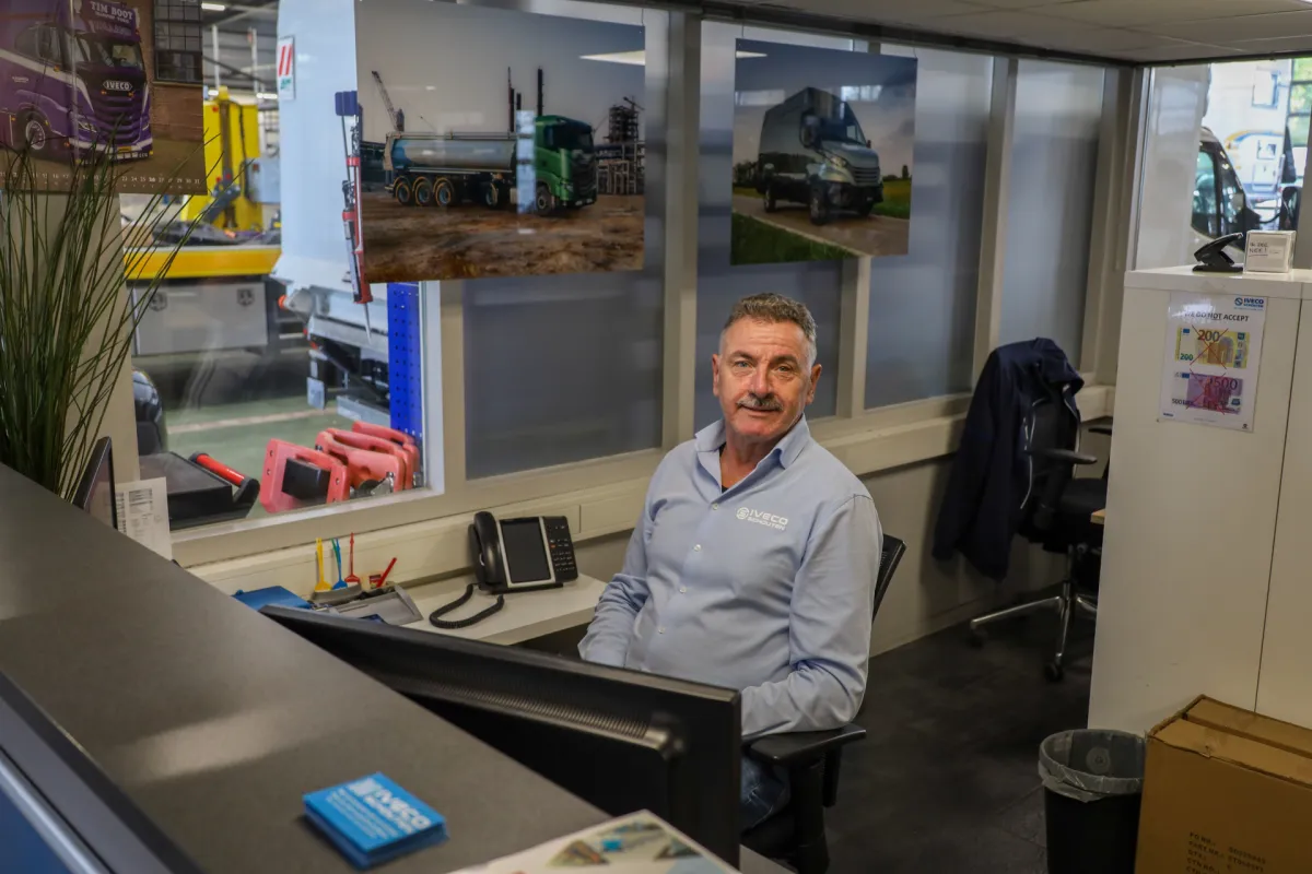 Vestigingsmanager achter computer, met vrachtwagenposters op de achtergrond